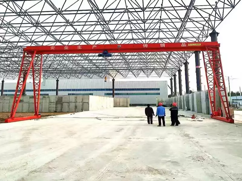 Single girder gantry crane in a factory yard, lifting heavy metal workpieces, demonstrating practical material transfer in industrial environments